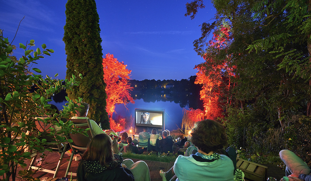 Open Air Kino direkt am See, die Besucher sitzen auf einem terrassierten Gelände und schauen auf die Leinwand und dem Wasser.